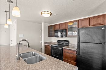 A kitchen with a black refrigerator and a granite countertop.